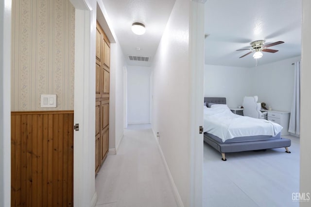 corridor featuring light wood-style floors, wainscoting, visible vents, and wallpapered walls