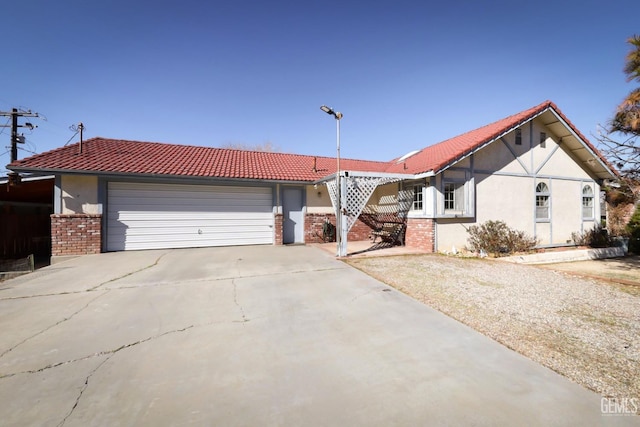 view of front facade with a garage, driveway, brick siding, a tiled roof, and stucco siding