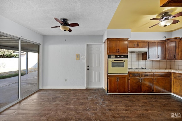 kitchen featuring tile countertops, white gas cooktop, dark wood-type flooring, oven, and decorative backsplash