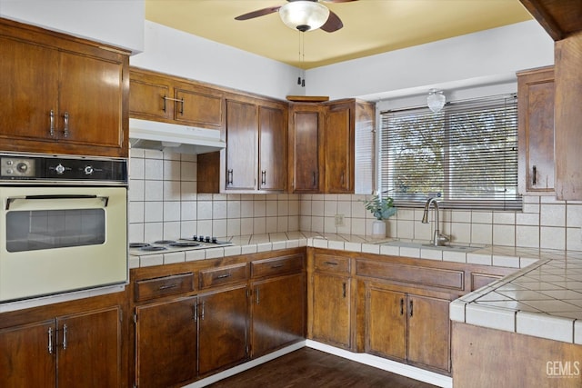 kitchen featuring dark hardwood / wood-style flooring, backsplash, white appliances, sink, and tile counters