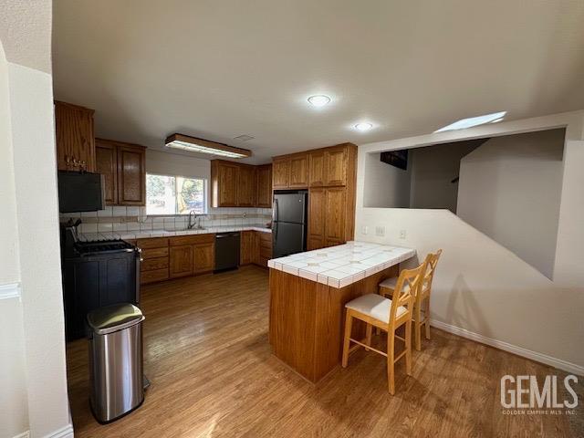 kitchen with backsplash, black appliances, tile counters, kitchen peninsula, and a breakfast bar area