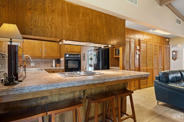 2924 Elm St, Bakersfield, CA 93301 - kitchen featuring black appliances, decorative backsplash, brown cabinets, light tile patterned floors, and a peninsula