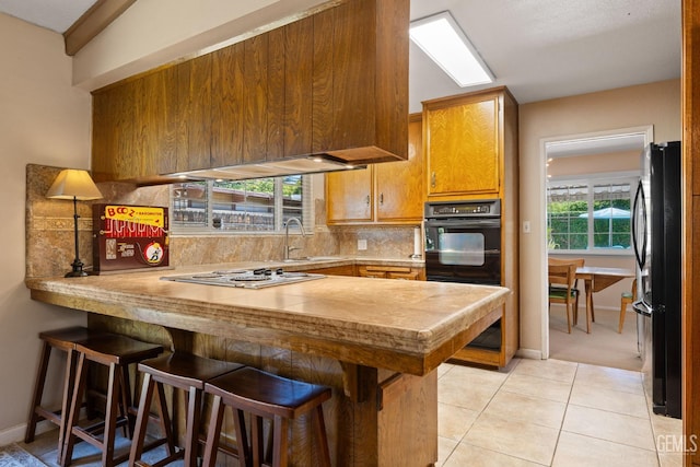 2924 Elm St, Bakersfield, CA 93301 - kitchen featuring black appliances, a peninsula, backsplash, a kitchen bar, and light countertops