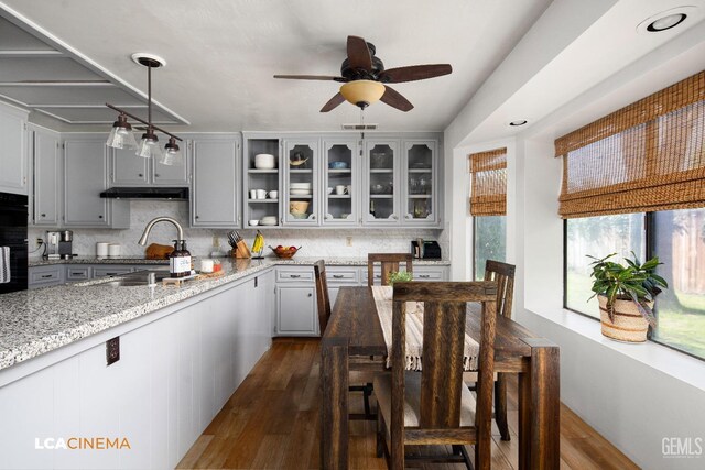 kitchen featuring tasteful backsplash, visible vents, light stone countertops, under cabinet range hood, and dark wood-style floors