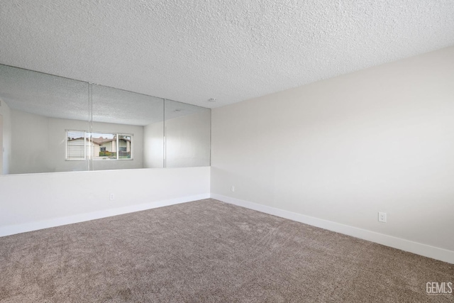 empty room with carpet, baseboards, and a textured ceiling