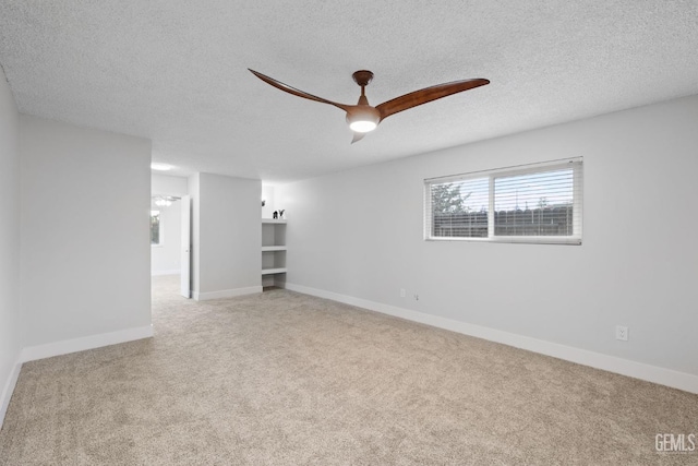 empty room with baseboards, a textured ceiling, a ceiling fan, and light colored carpet