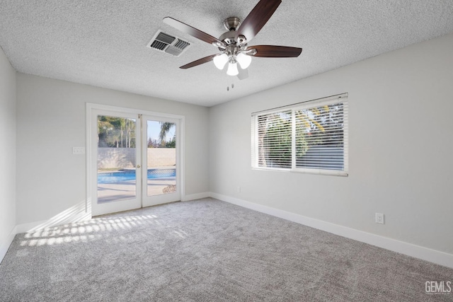 carpeted empty room with a textured ceiling, ceiling fan, visible vents, and baseboards