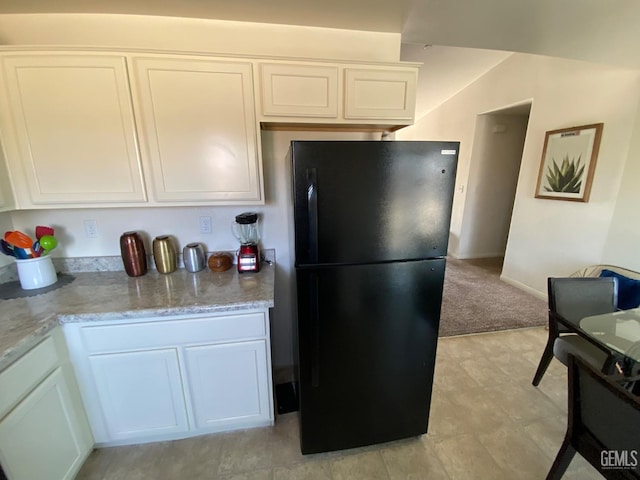 kitchen with light stone counters, white cabinets, freestanding refrigerator, and light floors
