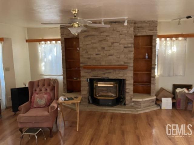 sitting room featuring a wood stove, ceiling fan, rail lighting, and hardwood / wood-style flooring