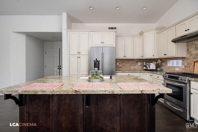 kitchen with stainless steel appliances, light stone countertops, a kitchen island, and decorative backsplash