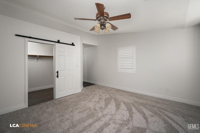 unfurnished bedroom featuring lofted ceiling, ceiling fan, carpet floors, a barn door, and a closet