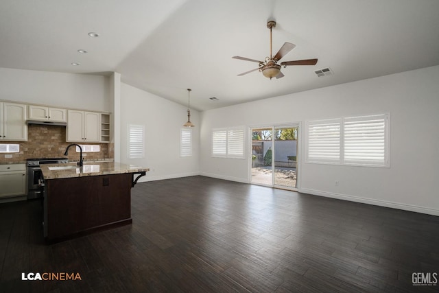 kitchen with a breakfast bar, stainless steel range oven, hanging light fixtures, a center island with sink, and backsplash