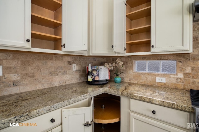 kitchen featuring white cabinetry, backsplash, built in desk, and light stone countertops