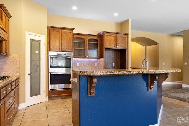 kitchen featuring stainless steel appliances, a kitchen breakfast bar, backsplash, and light stone counters