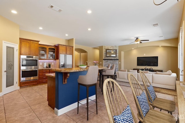 kitchen with a ceiling fan, brown cabinets, a breakfast bar area, appliances with stainless steel finishes, and visible vents