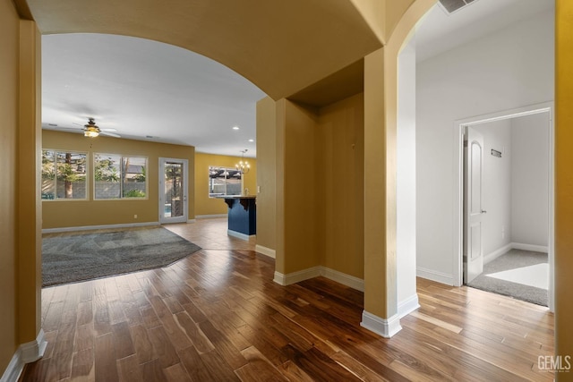 hall featuring arched walkways, wood finished floors, and baseboards