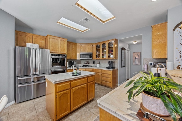 8628 Sandpines Dr, Bakersfield, CA 93312 - kitchen featuring appliances with stainless steel finishes, tasteful backsplash, glass insert cabinets, a kitchen island, and a skylight