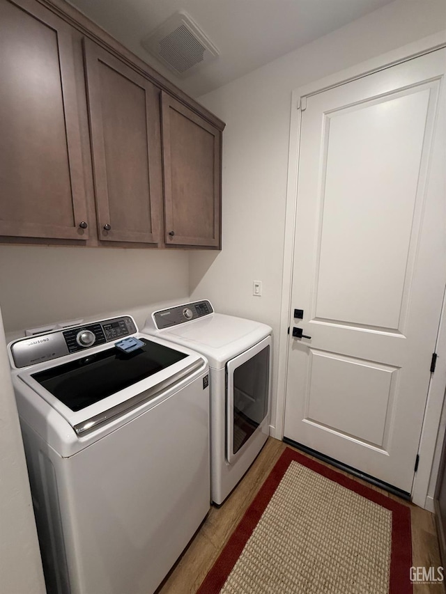 washroom with cabinets, wood-type flooring, and separate washer and dryer