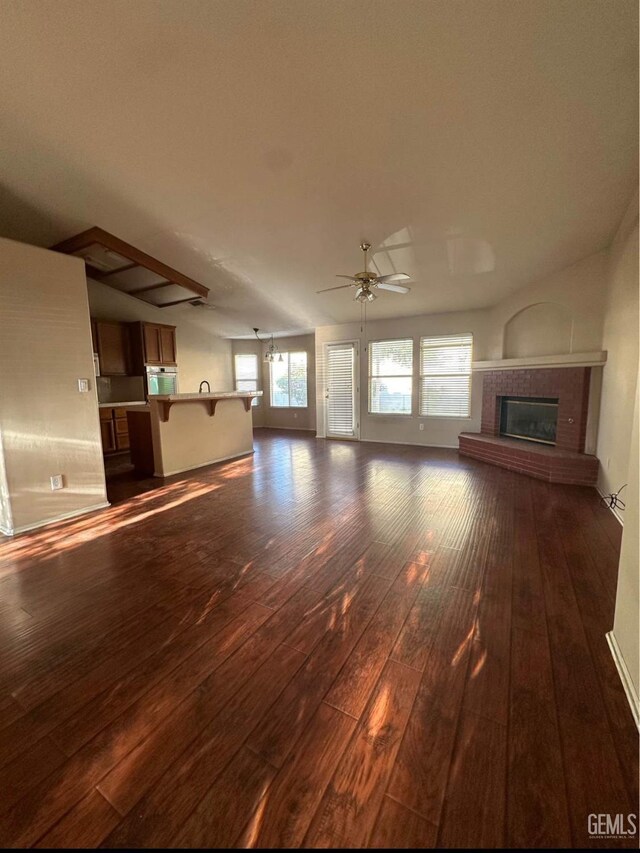 unfurnished living room featuring ceiling fan, dark wood-type flooring, and a brick fireplace