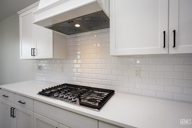 kitchen featuring range hood, stainless steel gas stovetop, white cabinetry, and light countertops
