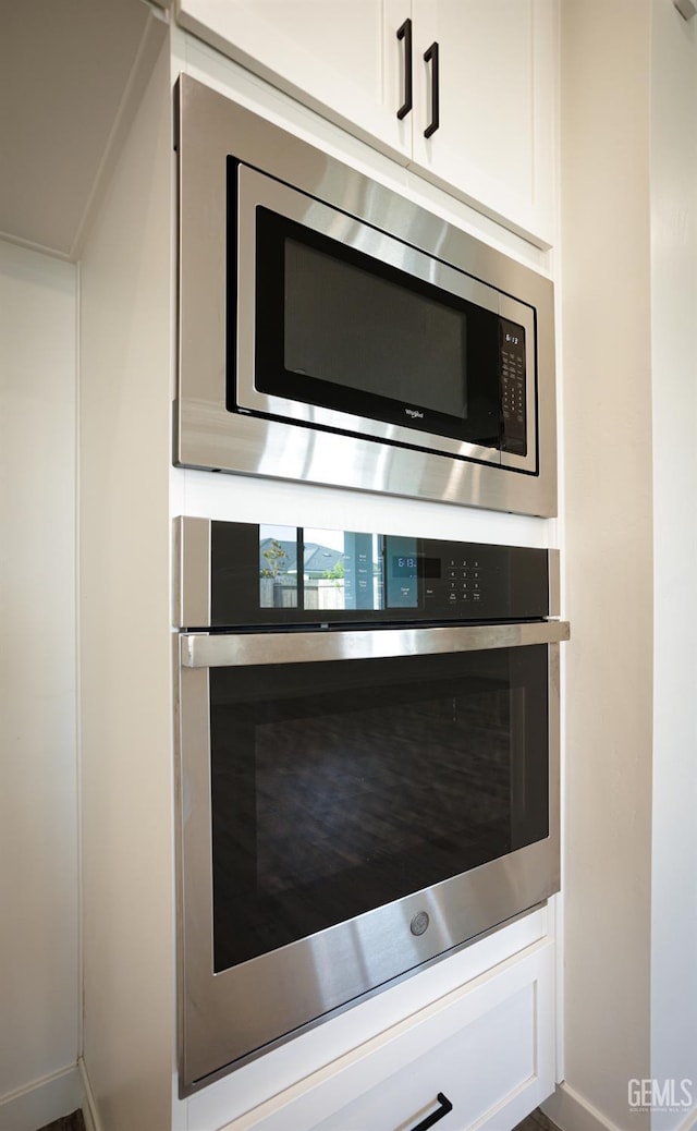 kitchen view of stainless steel appliances, baseboards, and white cabinetry