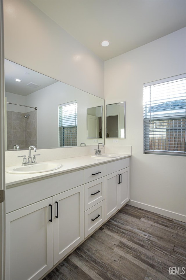 full bath featuring double vanity, plenty of natural light, wood finished floors, a tile shower, and recessed lighting