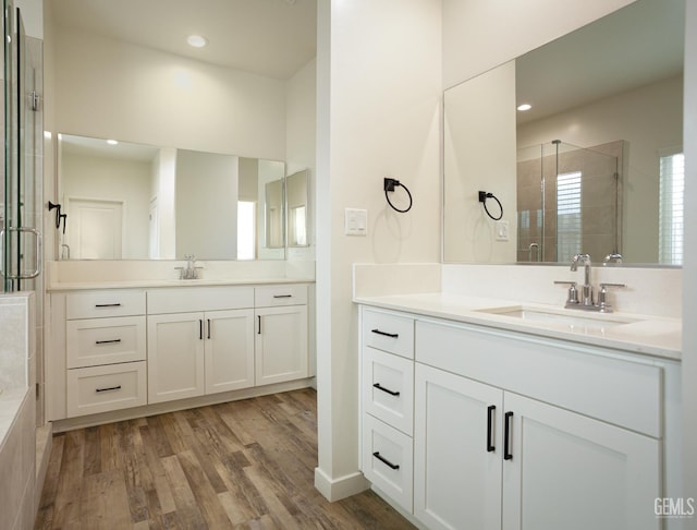 full bathroom featuring a stall shower, two vanities, wood finished floors, and recessed lighting