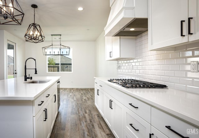 kitchen with a sink, appliances with stainless steel finishes, premium range hood, tasteful backsplash, and a chandelier