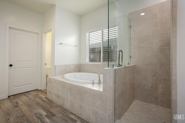 full bathroom with wood finished floors, a bath, a shower stall, and toilet