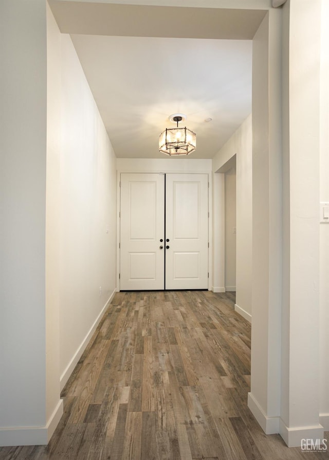 hall featuring wood finished floors, a chandelier, and baseboards