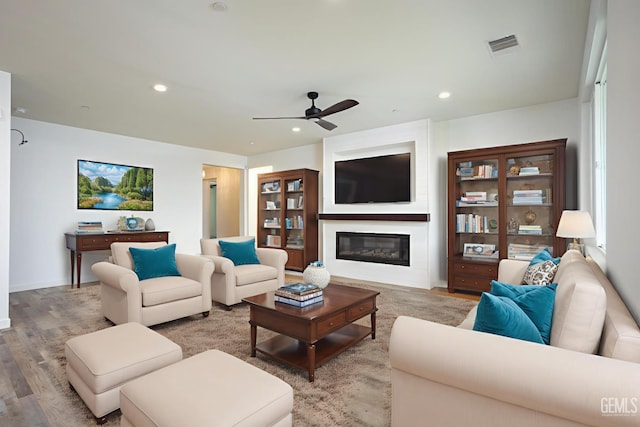 living room with ceiling fan, light wood-style floors, a glass covered fireplace, recessed lighting, and baseboards