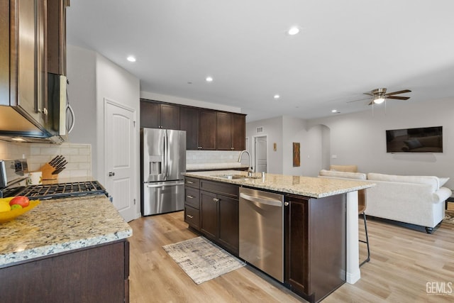 kitchen with a sink, arched walkways, light wood-style floors, dark brown cabinetry, and appliances with stainless steel finishes
