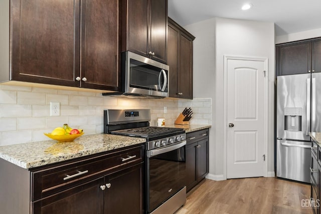 kitchen featuring light wood-style floors, light stone countertops, dark brown cabinetry, decorative backsplash, and appliances with stainless steel finishes