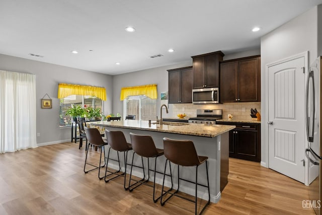 kitchen featuring a sink, tasteful backsplash, a center island with sink, a kitchen bar, and appliances with stainless steel finishes