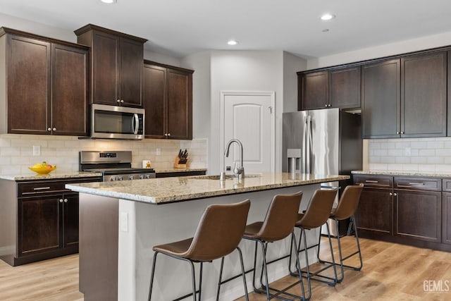 kitchen featuring a kitchen island with sink, a kitchen breakfast bar, a sink, light stone countertops, and appliances with stainless steel finishes