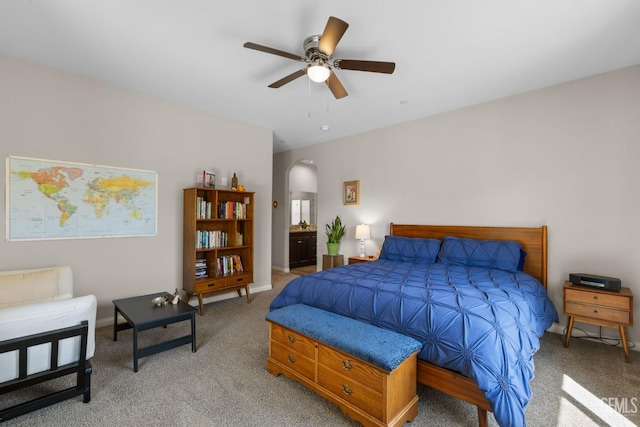 bedroom featuring light carpet, ensuite bathroom, arched walkways, and ceiling fan