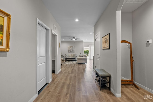 hallway featuring arched walkways, light wood-style flooring, baseboards, visible vents, and recessed lighting
