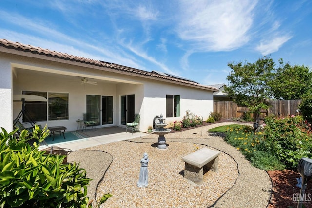 back of property featuring roof mounted solar panels, fence, stucco siding, a patio area, and ceiling fan