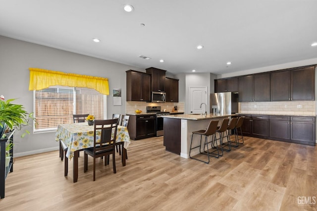 kitchen with stainless steel appliances, a kitchen breakfast bar, dark brown cabinets, light wood-type flooring, and visible vents