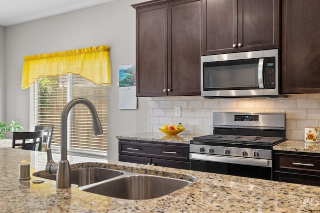 kitchen featuring light stone counters, tasteful backsplash, a sink, dark brown cabinetry, and appliances with stainless steel finishes
