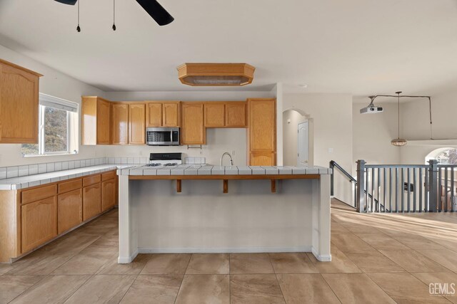 408 Brite Meadow Ct, Bakersfield, CA 93308 - kitchen featuring stainless steel microwave, stove, ceiling fan, tile countertops, and a sink