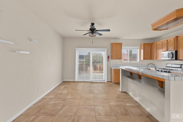 408 Brite Meadow Ct, Bakersfield, CA 93308 - kitchen featuring range, tile countertops, stainless steel microwave, a ceiling fan, and baseboards