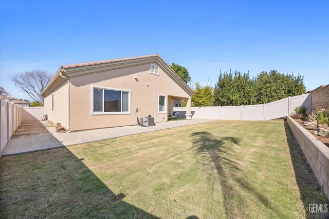rear view of house with a tiled roof, a lawn, a fenced backyard, a patio, and stucco siding