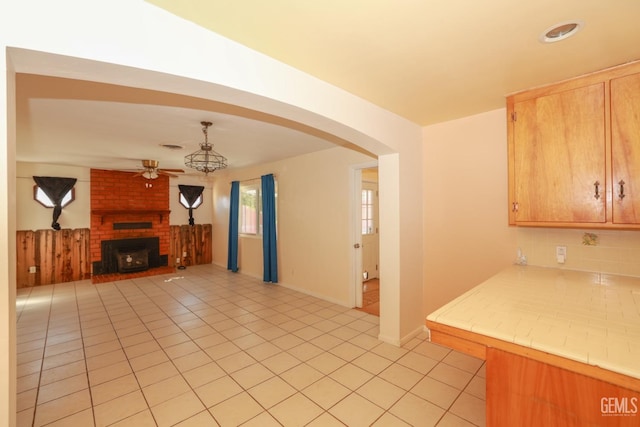 kitchen featuring ceiling fan, pendant lighting, tile countertops, a fireplace, and light tile patterned flooring