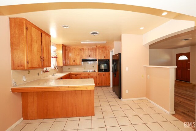 kitchen with tasteful backsplash, kitchen peninsula, light tile patterned floors, and black appliances