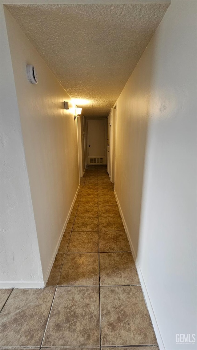 hall with tile patterned flooring, baseboards, visible vents, and a textured ceiling