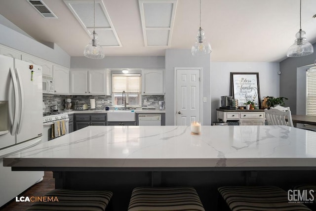 kitchen with white appliances, light stone counters, visible vents, a sink, and white cabinetry