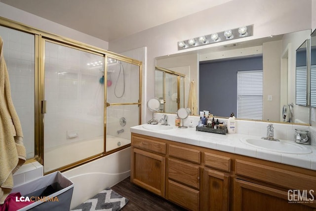 bathroom with double vanity, combined bath / shower with glass door, wood finished floors, and a sink