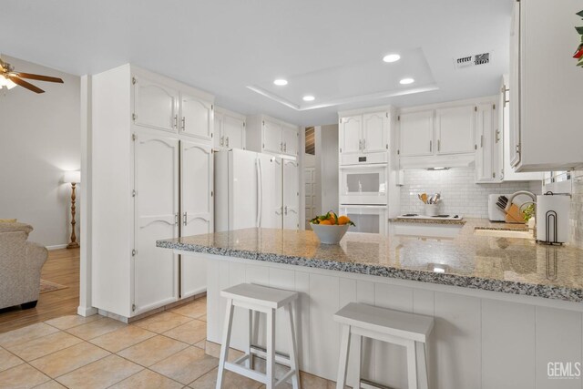 2700 Hoad Ln, Bakersfield, CA 93309 - kitchen featuring a sink, a peninsula, white appliances, a raised ceiling, and light stone counters