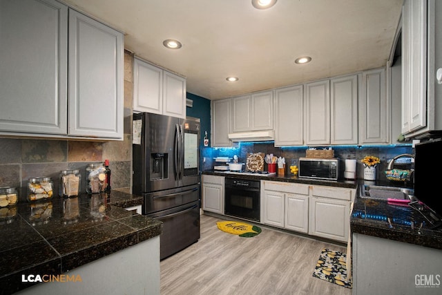 kitchen featuring tile countertops, stainless steel fridge with ice dispenser, a sink, under cabinet range hood, and black oven